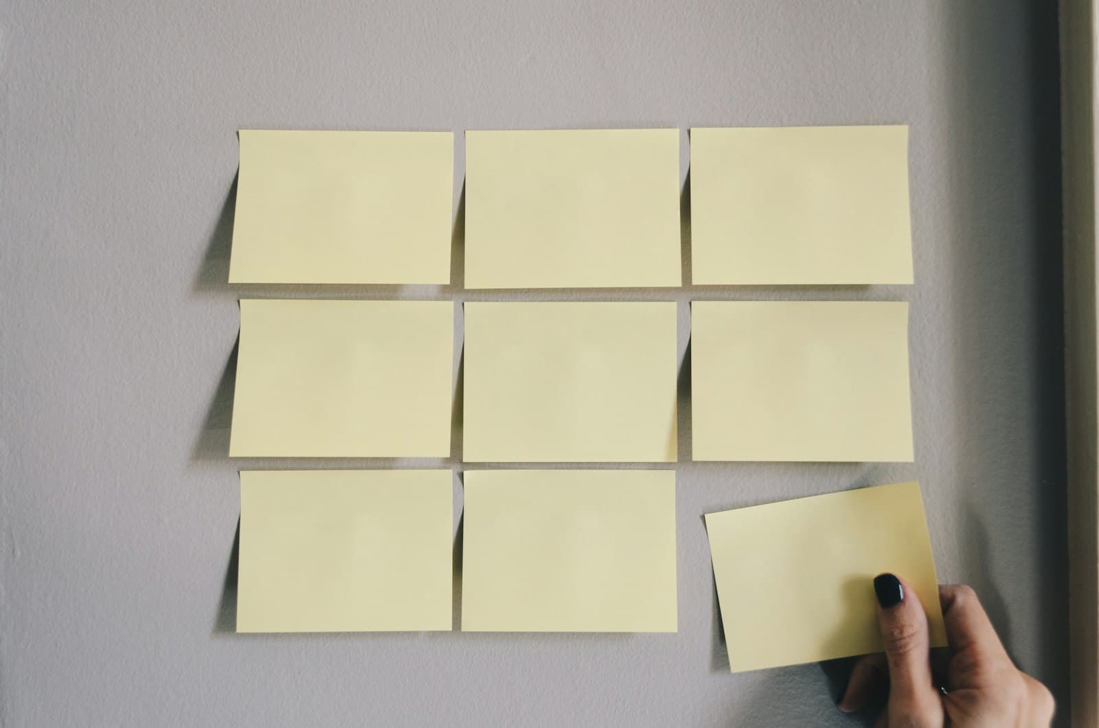 Hand plakt gele post-its in een raster op een muur
