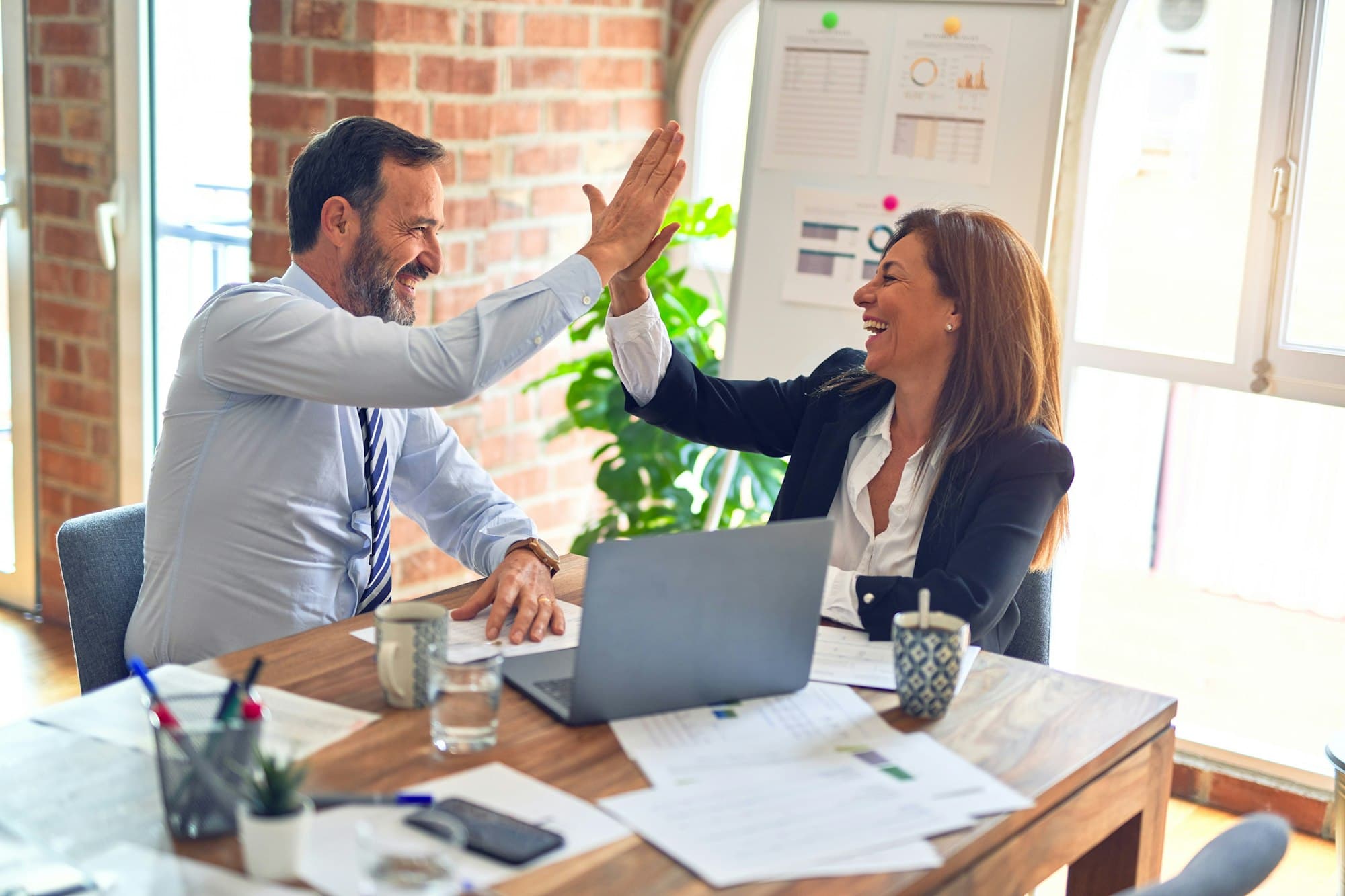 Twee collega's geven elkaar een high five achter een laptop