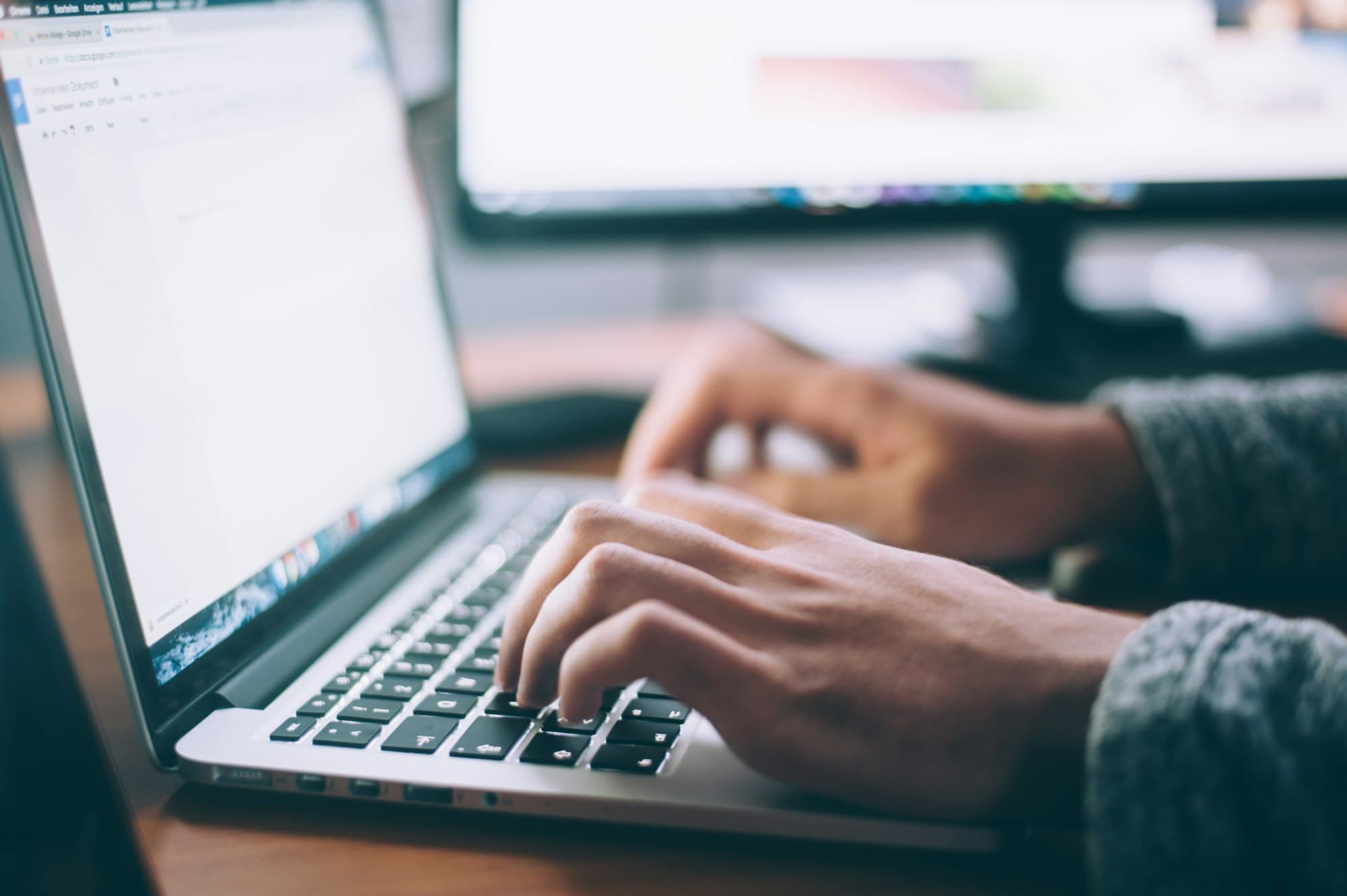 Handen typen op een laptop met een tweede scherm op de achtergrond