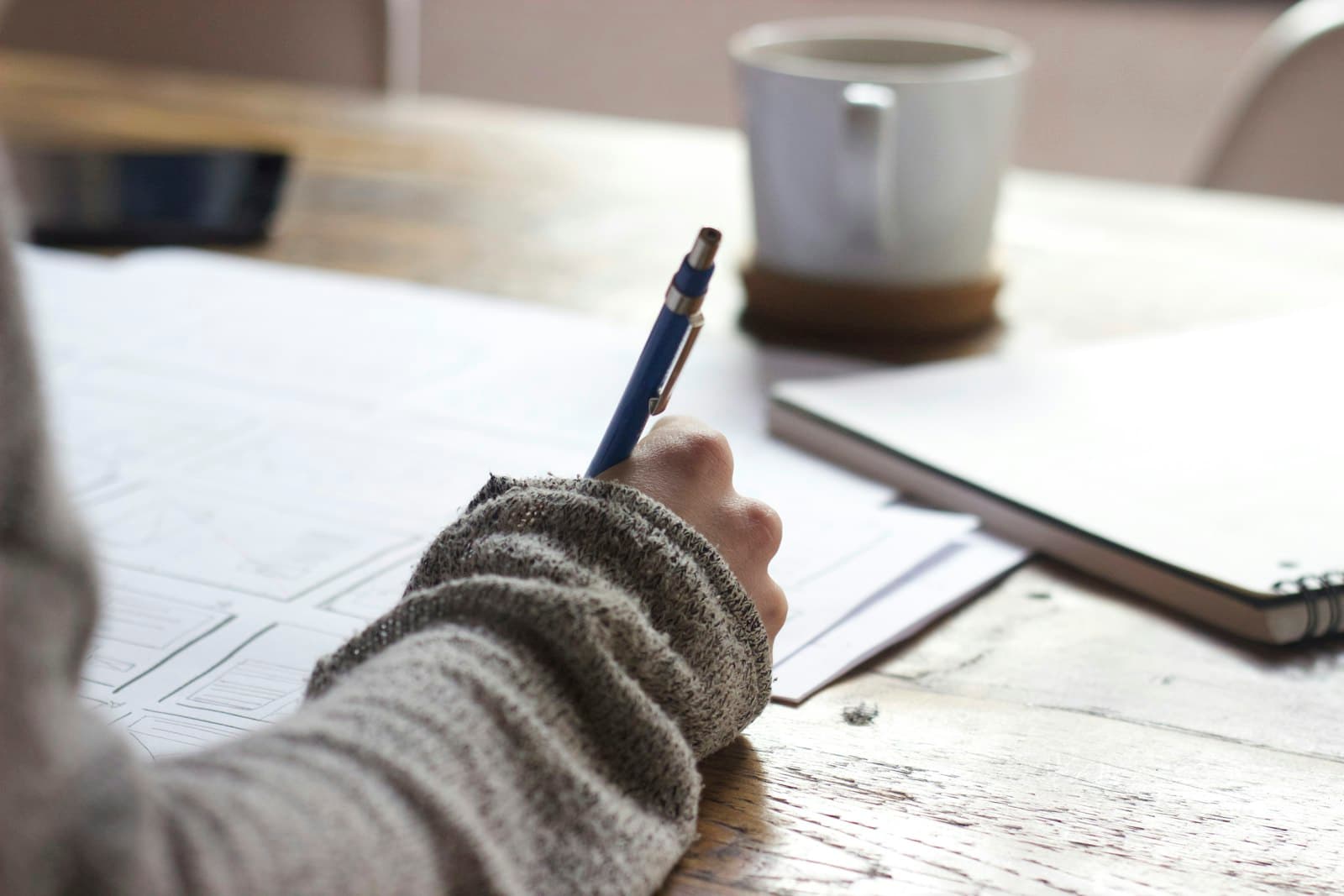Hand die een processchets uitwerkt op papier, naast een kop koffie